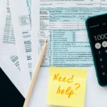 Close-up of tax forms with a calculator and a note asking for assistance.