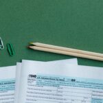 U.S. tax forms with pencils and paperclips on green surface in a flat lay setup.