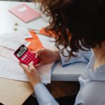Adult woman working with receipts and a bright pink calculator at a desk, focusing on finances.